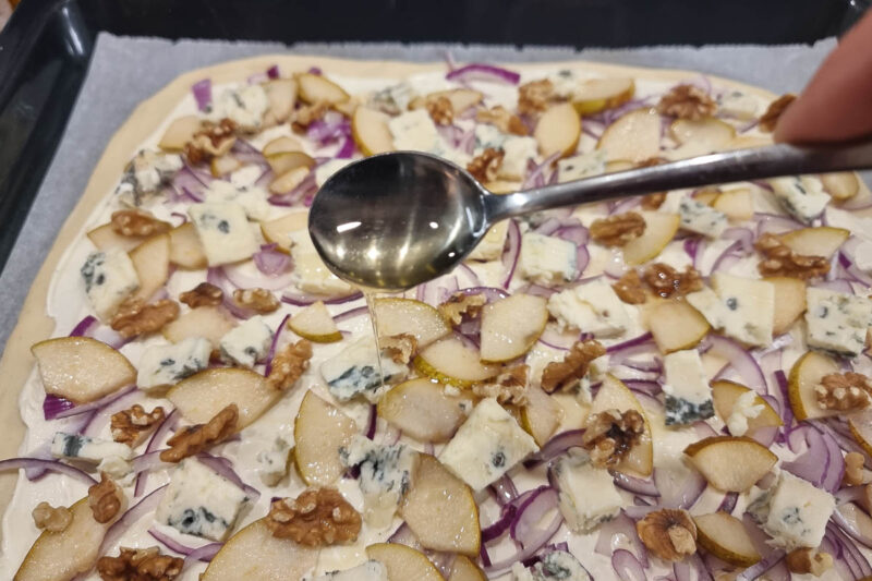 Der Flammkuchen wird mit Honig beträufelt
