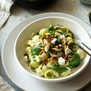 Pasta mit Erbsen Feta und Basilikum auf weißem Teller