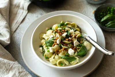 Pasta mit Erbsen Feta und Basilikum auf weißem Teller